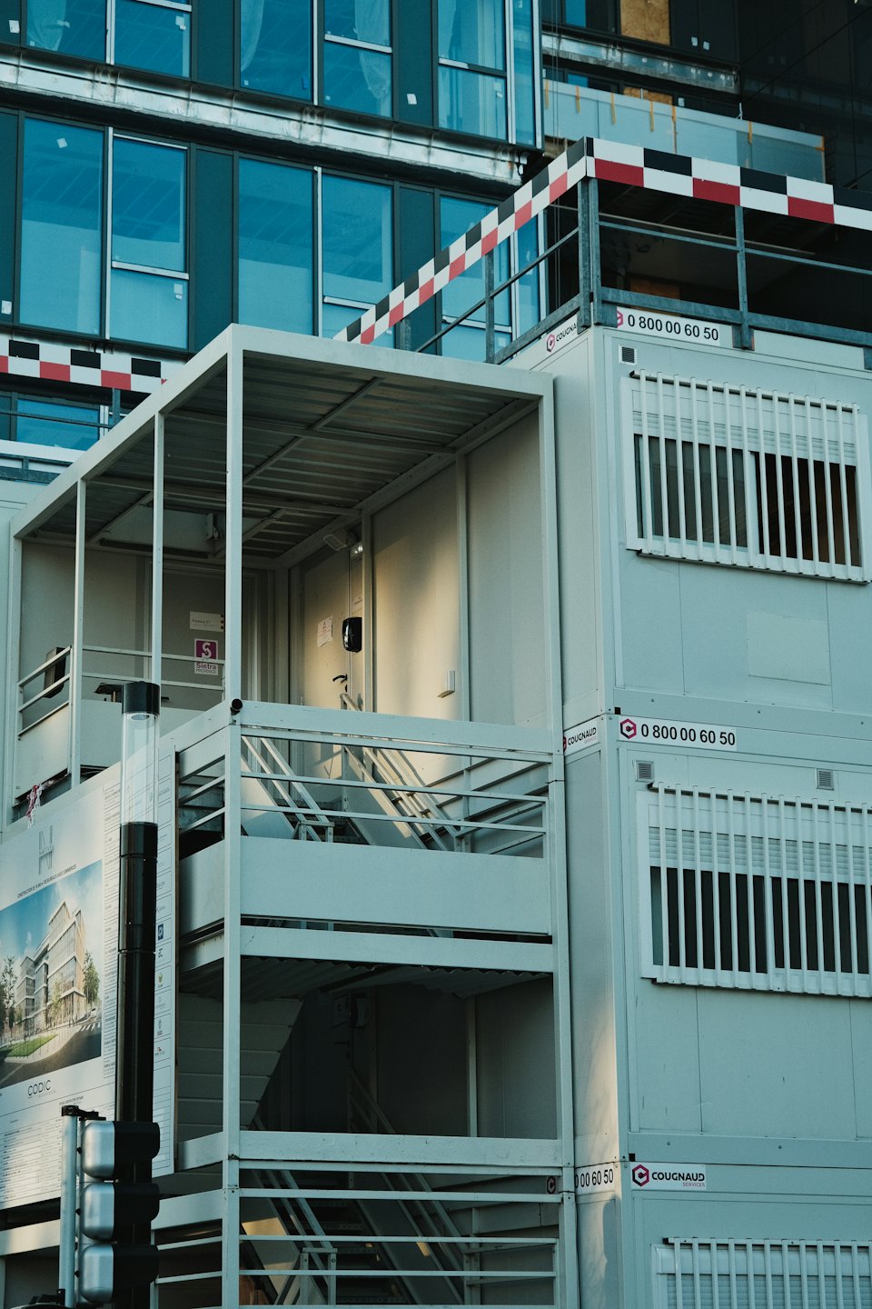 Stacked modular construction offices stand before a modern glass building.